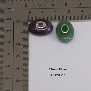 Puede incluir: Dos colgantes ovalados de piedras preciosas. Uno es morado con un centro morado claro, el otro es verde con un centro verde. Ambos tienen bordes de metal dorado. Miden 21mm x 13mm.