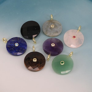 May include: A collection of gemstone pendants in various colors, including black, blue, purple, pink, brown, green, and gray. Each pendant is round with a faceted surface and a small gemstone in the center. Gold-colored bails are attached at the top.