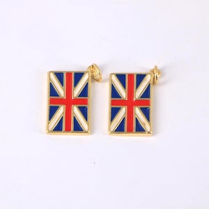 Puede incluir: Dos colgantes rectangulares dorados con el diseño de la bandera de la Union Jack. El diseño de la bandera incluye esmalte rojo, blanco y azul. Cada colgante tiene un pequeño lazo dorado en la parte superior para sujetarlo a una cadena o pulsera.