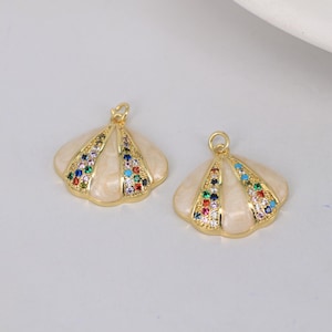 Op de afbeelding: Twee gouden schelpvormige bedels met wit emaille en kleurrijke strass steentjes.
