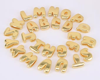 May include: A collection of gold-colored alphabet letter charms. Each letter is in a rounded, bubble-like font. The letters are arranged in a circular pattern against a white background. These charms are suitable for jewelry making and crafting.
