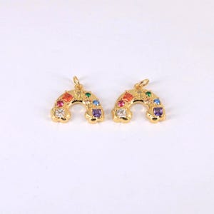 May include: Two gold-coloured rainbow charms with colourful square-cut gemstones. The charms have a small loop at the top for hanging. The gemstones are red, orange, yellow, green, blue, purple, and white.