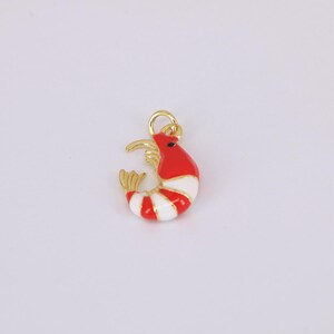 May include: A gold-colored shrimp charm with red and white stripes. The charm has a gold loop for attaching to a necklace or bracelet. The shrimp's body is red with white stripes, and it has a gold head and tail.