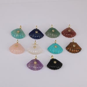 May include: A collection of seashell pendants in various colors, including turquoise, navy, green, and brown. Each pendant features a gold-colored bail and a small, round, clear stone in the center. The pendants are displayed against a white background.
