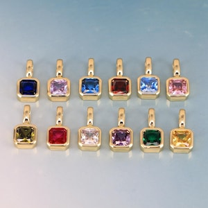 May include: A collection of twelve gold-colored pendants, each featuring a square-cut gemstone in various colors, including blue, pink, green, and red. The pendants are arranged in two rows against a light blue background.
