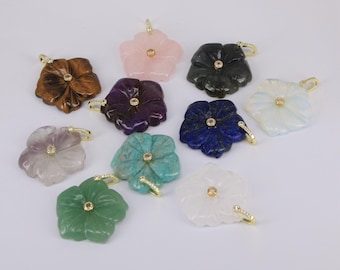 May include: A collection of gemstone flower pendants in various colors, including pink, green, purple, and blue. Each pendant features a gold-colored bail and a small, round accent stone in the center. The pendants are displayed against a white background.