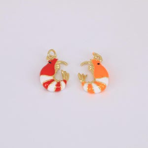 May include: Two colorful shrimp charms. One is red and white striped, the other is orange and white striped. Both have gold-colored accents and a small loop for attaching to jewelry or other crafts.