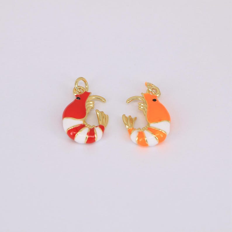 May include: Two colorful shrimp charms. One is red and white striped, the other is orange and white striped. Both have gold-colored accents and a small loop for attaching to jewelry or other crafts.