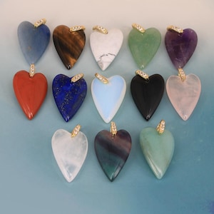 Puede incluir: Una colección de trece colgantes de piedras preciosas en forma de corazón de varios colores, incluyendo azul, marrón, blanco, verde, morado, rojo, negro y rosa. Cada colgante tiene un enganche de metal dorado en la parte superior con cristales.