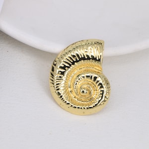 May include: A gold-colored seashell pendant with a detailed spiral design. The pendant is made of metal and has a smooth, polished finish.