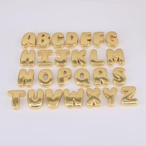 May include: A complete set of gold-colored, bubble-style alphabet letters. Each letter is individually crafted with a shiny, metallic finish. The letters are arranged in alphabetical order, A through Z.