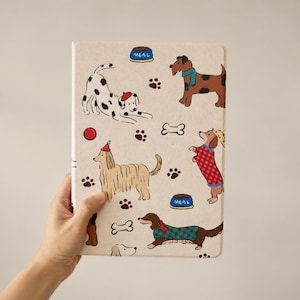 May include: A rectangular notebook with a light beige cover featuring a repeating pattern of various dog breeds, including a dalmatian, a brown dog with a blue scarf, and a dachshund in a red plaid sweater, alongside blue meal bowls and bones.