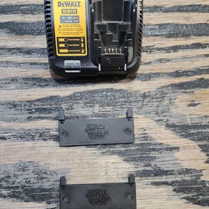 May include: A black DeWalt DCB115 12V/20V MAX Lithium Ion battery charger with a yellow label. The charger is on a wooden surface with two black plastic covers.