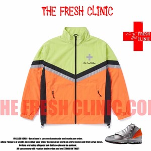 May include: A neon yellow and orange windbreaker jacket with a black full-length zipper, black side panels, and a reflective chevron stripe. The chest features a grey cross logo and the text The Fresh Clinic in a cursive black font.