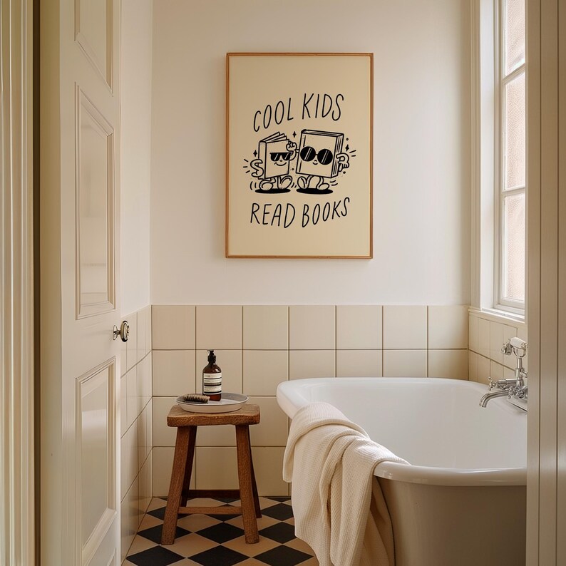 K&ouml;nnte beinhalten: Eine Schwarzwei&szlig;illustration von zwei B&uuml;chern, die Sonnenbrillen tragen und gehen, mit dem Text "Cool Kids Read Books" dar&uuml;ber. Die Illustration ist gerahmt und h&auml;ngt an einer Wand in einem Badezimmer mit einer wei&szlig;en Badewanne und einem Holzhocker.