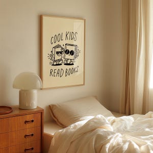 K&ouml;nnte beinhalten: Ein beigefarbener gerahmter Druck mit schwarzem Text und Illustrationen. Der Text lautet "Cool Kids Read Books". Die Illustration zeigt zwei B&uuml;cher mit Sonnenbrillen und Armen und Beinen.