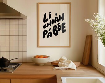 Puede incluir: Una impresión artística enmarcada con las palabras "Liám Chiáh Páboe" en letras negras en negrita. La impresión está en un marco de madera clara y cuelga en un entorno de cocina. La cocina tiene una encimera de madera, un cuenco de naranjas y un fregadero blanco.