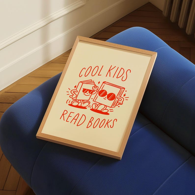K&ouml;nnte beinhalten: Ein beigefarbener gerahmter Druck mit dem Text "Cool Kids Read Books" in Rot. Der Druck zeigt eine Comic-Illustration von zwei B&uuml;chern mit Sonnenbrillen und Armen und Beinen.