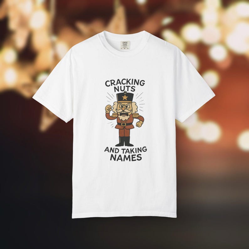 Vintage style Christmas shirt, with rubber hose style nut cracker cartoon character, with "Cracking Nuts and Taking Names" caption, on white comfort colors tee.