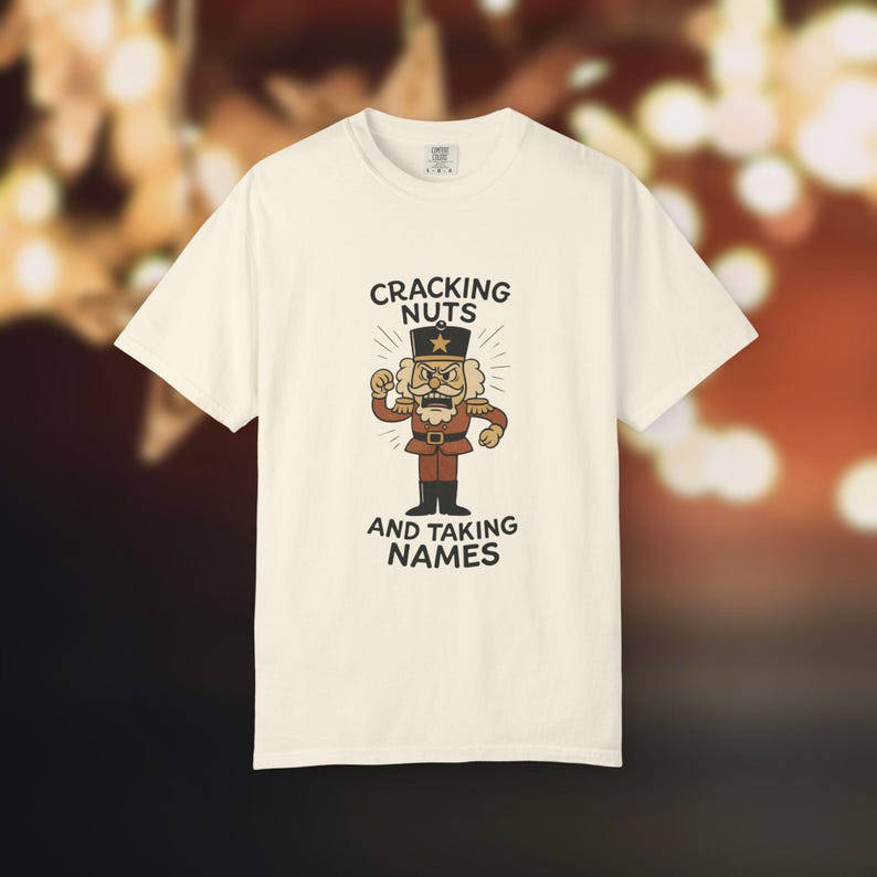 Vintage style Christmas shirt, with rubber hose style nut cracker cartoon character, with "Cracking Nuts and Taking Names" caption, on ivory comfort colors tee.