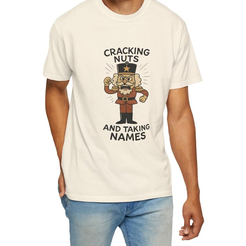 Vintage style Christmas shirt, with rubber hose style nut cracker cartoon character, with "Cracking Nuts and Taking Names" caption, on model wearing ivory comfort colors tee.