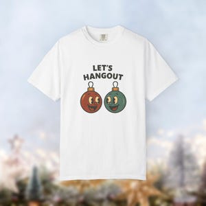 May include: White t-shirt featuring the text "LET'S HANGOUT" above two cartoon Christmas bauble characters. One bauble is red, the other green, both with smiling faces and gold-coloured metal caps.