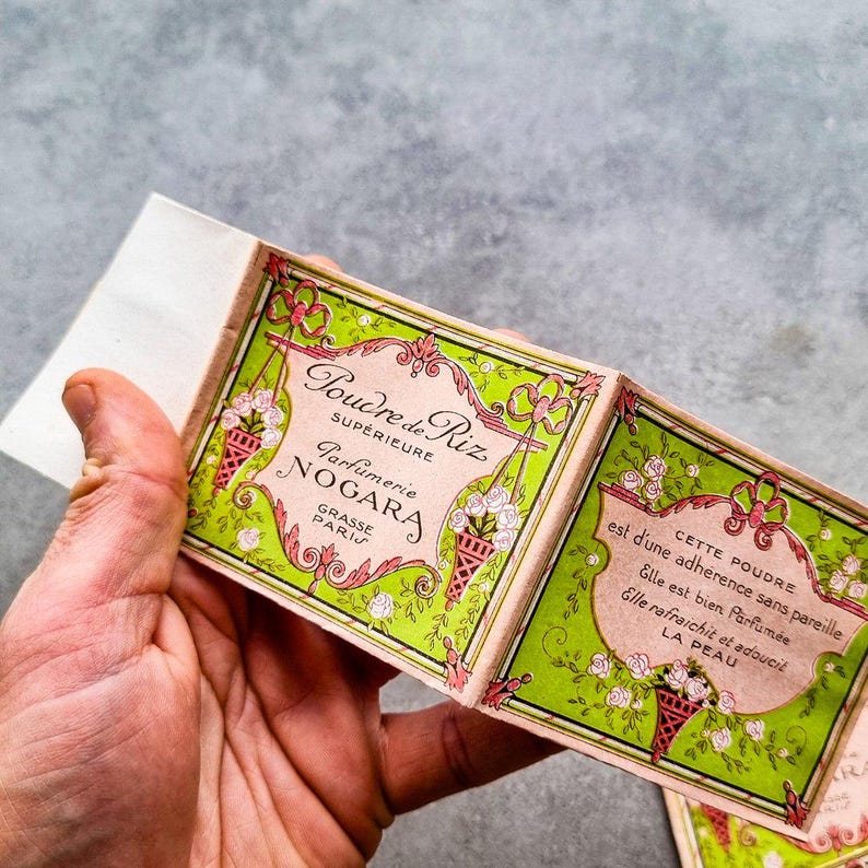 May include: A vintage box of face powder with a green and pink floral design. The box is labeled "Poudre de Riz Superieure Parfumerie Nogara Grasse Paris".