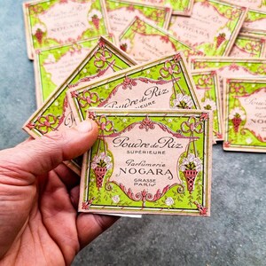 May include: A stack of vintage green and pink paper boxes with a floral design. The top box reads "Poudre de Riz Superieure Parfumerie Nogara Grasse Paris".