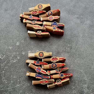 Könnte beinhalten: Zwei Stapel Vintage-Zigarrenbänder. Die Bänder weisen goldene, rote, blaue und weiße Farben mit verschiedenen Designs und Texten auf, darunter das Wort "Patron". Die Bänder sind auf einer grauen Oberfläche angeordnet.