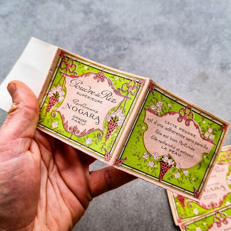 May include: A vintage box of face powder labeled "Poudre de Riz Superieure Parfumerie Nogara Grasse Paris". The box is green and pink with floral designs and the text "CETTE POUDRE est d'une adherence sans pareille Elle est bien Parfum&eacute;e Elle rafraichit et adoucit LA PEAU".