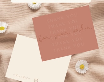 May include: A thank you note card with a brown background and the text "THANK YOU" repeated multiple times. The text "for your order" is written in cursive. The card is on a light brown fabric background with white flowers.