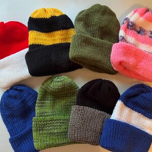 May include: Assortment of eight knitted winter hats in various colors and patterns, including red, white, black, yellow, green, blue, and pink.