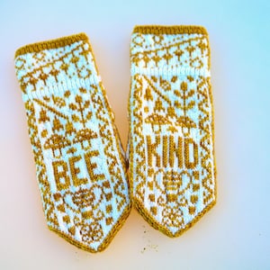 May include: A pair of white and gold knitted fingerless gloves with the words "Bee Kind" knitted into the design.