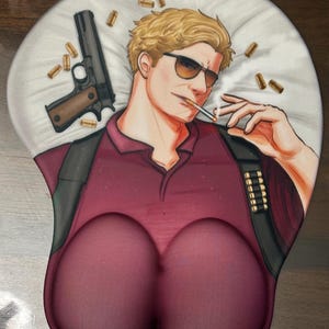 May include: Ergonomic mousepad featuring a stylized illustration of a man with sunglasses, smoking a cigarette, and a gun. The mousepad has a burgundy color scheme with a wrist rest.