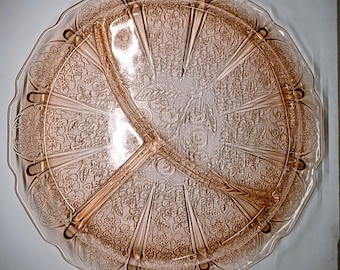 May include: A vintage pink glass serving platter with three divided sections. The platter has a scalloped edge and is decorated with a floral pattern. The design is etched into the glass, creating a textured surface. The platter is round and measures approximately 30 cm in diameter.