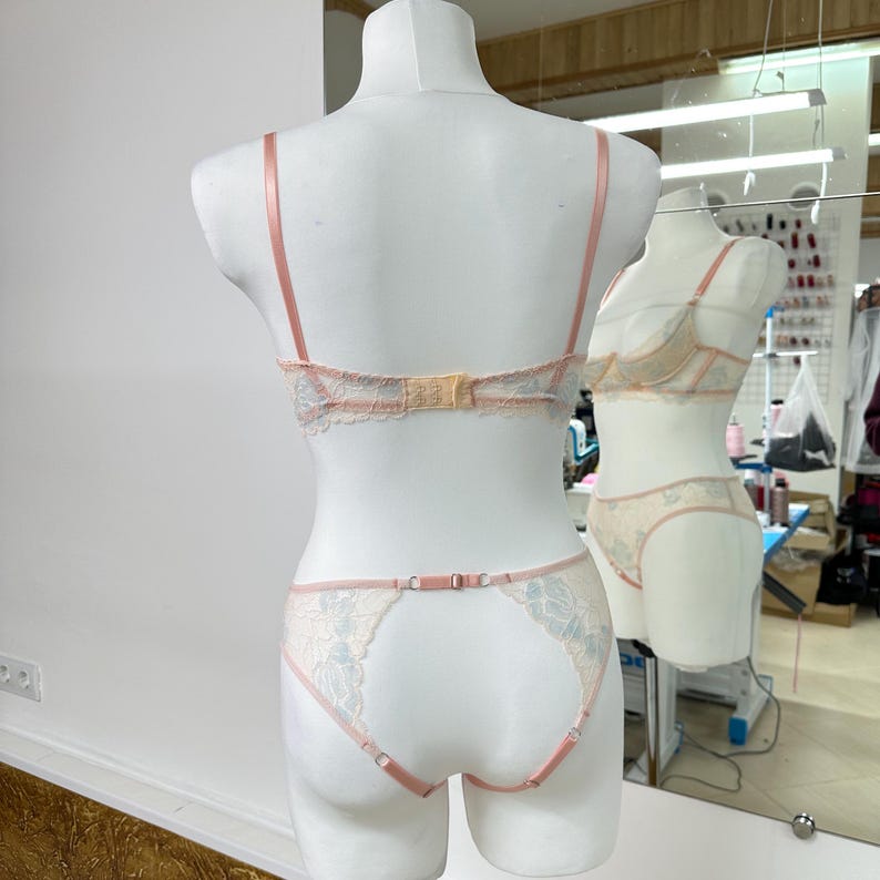 May include: A two-piece lingerie set featuring a bra and matching panties in pale peach and light blue lace. The bra has thin adjustable straps and a back hook closure. The panties feature a cut-out back design with thin straps.