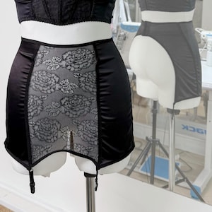 May include: Black satin and lace suspender belt with a floral pattern and adjustable straps.