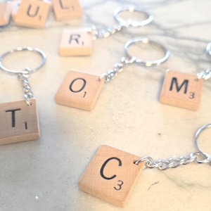 May include: A set of wooden letter tile keychains with silver key rings and chains. The tiles spell out the word "ROOM" and include the letters "T", "U", "L", "C", "M", and "O".