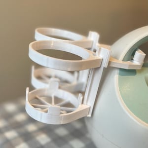 May include: White plastic bottle holder with three rings for bottles. The holder is attached to a light blue and white electric breast pump.