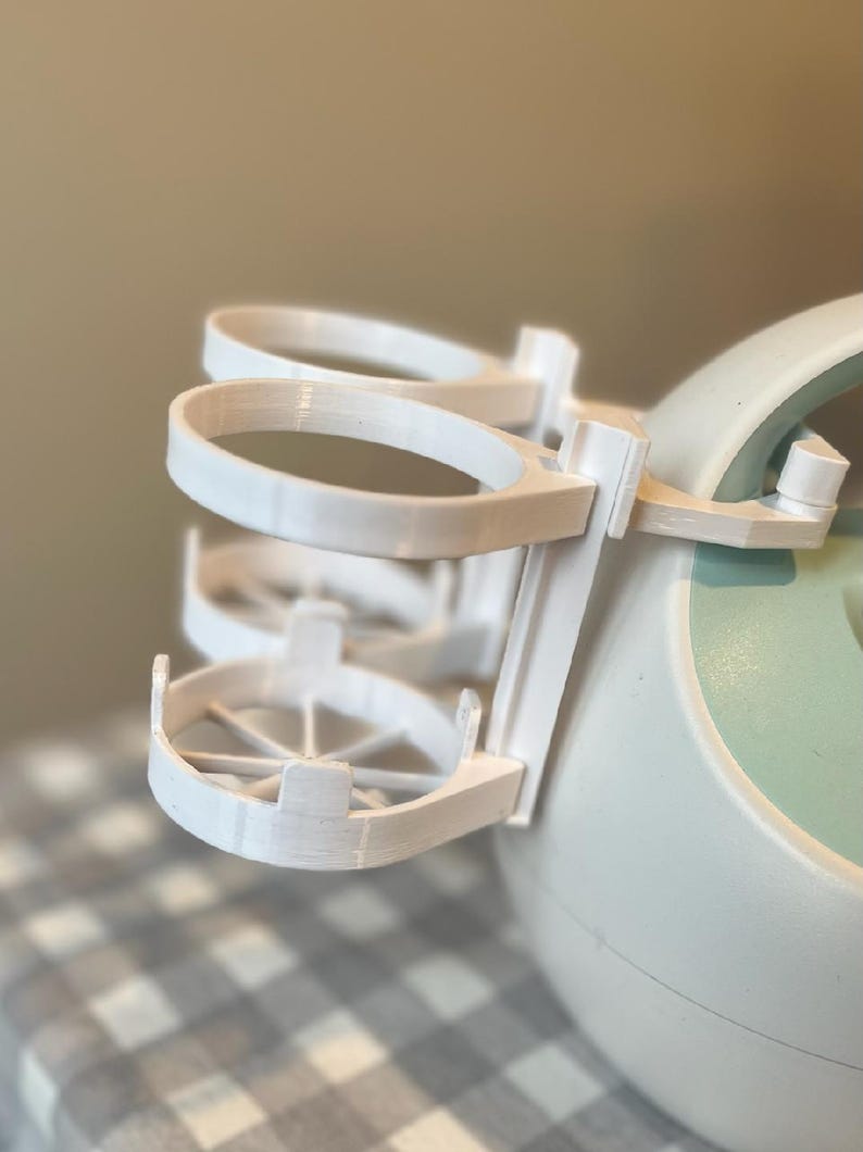 May include: White plastic bottle holder with three rings for bottles. The holder is attached to a light blue and white electric breast pump.