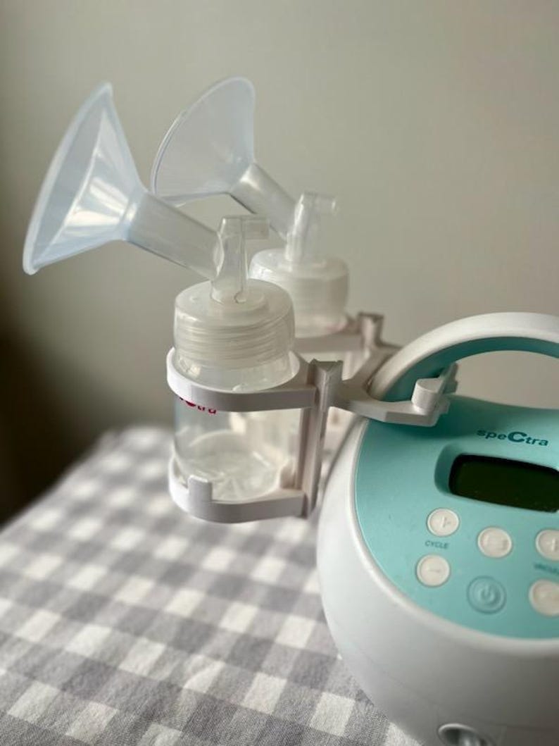 May include: A white and blue electric breast pump with a digital display and buttons. The pump has two clear bottles with white caps and two clear silicone funnels attached.