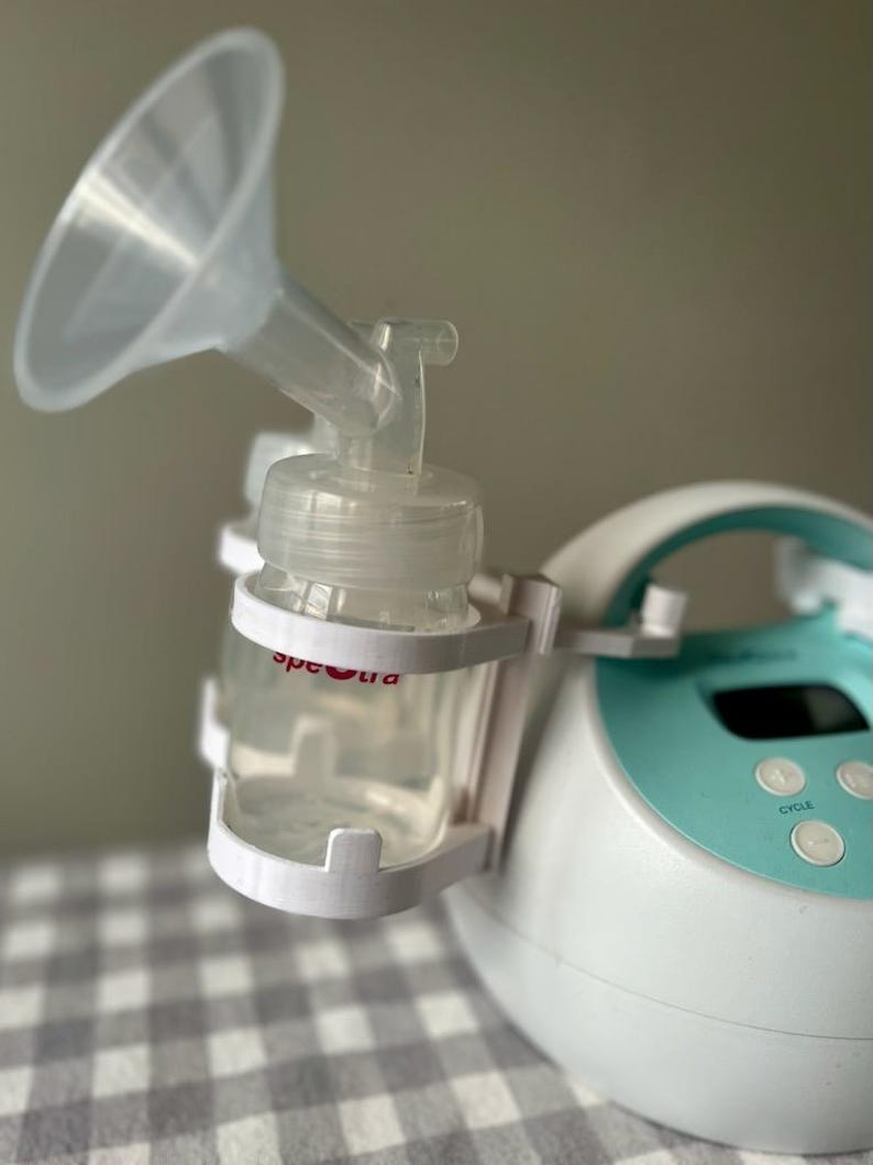 May include: A white and teal electric breast pump with a clear bottle and a funnel attached. The pump has a digital display with the word "cycle" on it.