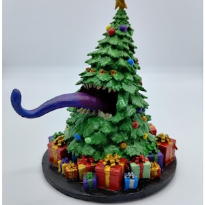 Op de afbeelding: Een grillige kerstboomfiguur met een groene, getextureerde body, versierd met kleurrijke ornamenten en een gouden ster. De boom heeft een gapende mond met een paarse tong. Cadeaus omringen de basis.