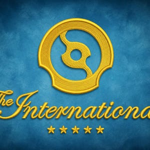 Puede incluir: Un emblema bordado dorado que presenta un diseño circular con un recorte central, colocado sobre el texto The International en letra cursiva, con cinco pequeñas estrellas doradas alineadas horizontalmente debajo sobre un fondo azul texturizado.