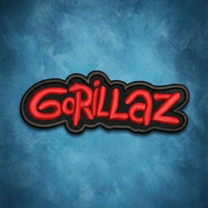 May include: Embroidered patch featuring the word "Gorillaz" in red, stylized lettering. The text is outlined in black and set against a blue background. The patch has a textured appearance, suggesting it is made of fabric.