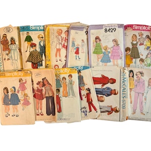 May include: A collection of vintage paper sewing patterns for children's clothing, featuring various Simplicity and McCall's brand envelopes with illustrations of dresses, pants, and jackets. The envelopes display model numbers like 8425, 8429, and 5709.
