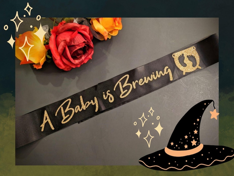May include: A black satin sash with gold glitter lettering that reads "A Baby is Brewing". The sash has a gold glitter cauldron with two footprints inside.