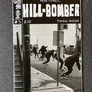 Op de afbeelding: Zwart-witte cover van een stripboek getiteld "Hill-Bomber" met nummer 3 en de prijs €10. De cover toont een groep mensen die skateboarden op straat.