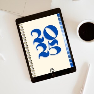 Peut inclure: Un agenda 2025 avec un thème bleu et blanc. L'agenda a une reliure spirale dorée et l'année 2025 est écrite en grandes lettres bleues. Le texte "2025 PLANNER" et "https://artbycharlie.kingshott.org" est écrit sous l'agenda.