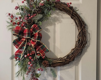 May include: A Christmas wreath made of woven twigs, adorned with red berries, pinecones, and evergreen sprigs. A large plaid bow with gold trim adds a festive touch. The wreath is displayed on a white door.